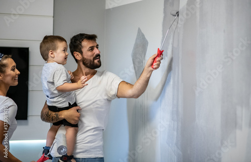 Father holds child in one hand and with the other hand paints walls in new apartment, renovates apartment for moving in photo