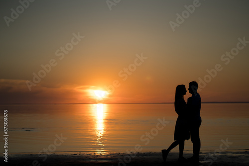 silhouette of a couple on the beach. Beautiful sunset of bright red orange color. Background for the travel website screensaver. Romantic picture, the concept of love.