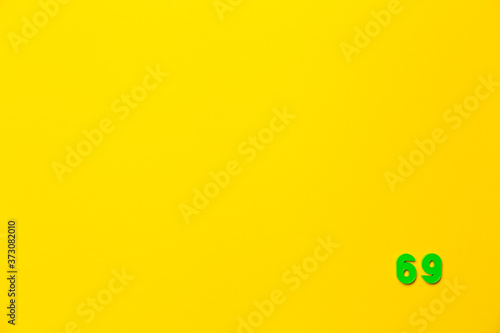A green plastic toy number sixty-nine is located in the lower right corner on a yellow background © Hanna