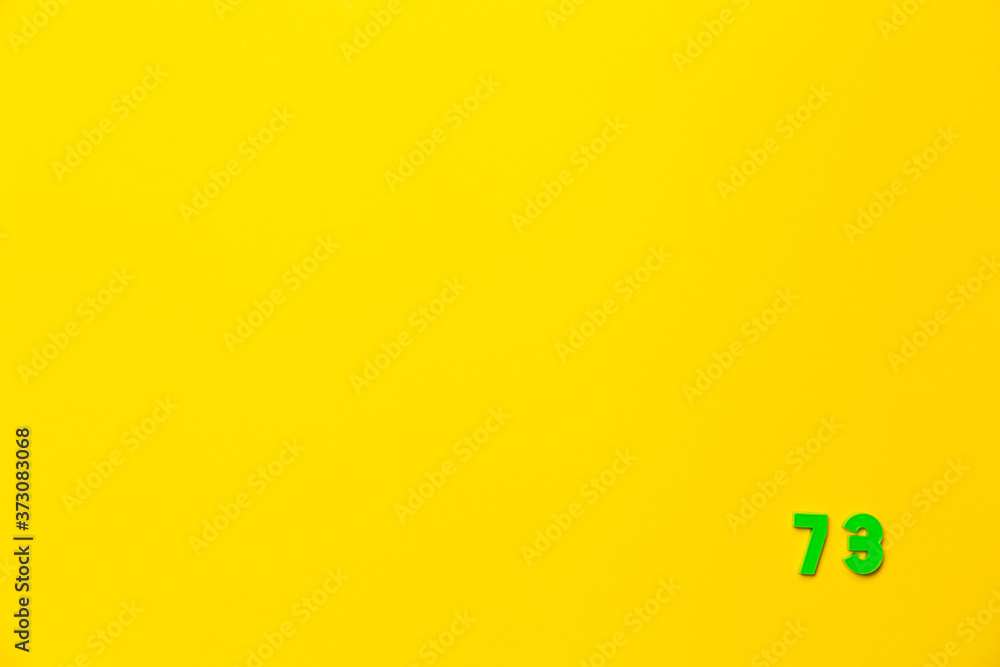 A green plastic toy number seventy-three is located in the lower right corner on a yellow background A green plastic toy number seventy-three is located in the lower right corner on a yellow background