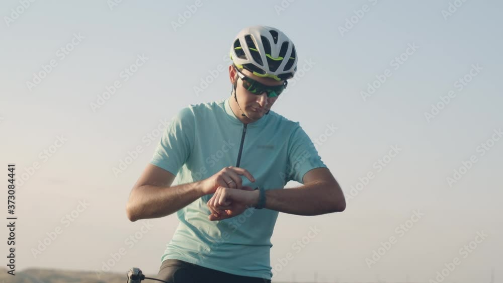 A male cyclist looks and clicks on a smart watch and rides away on a road bike. A Cycling guy checks his fitness bracelet and rides off on a bike on the highway A male cyclist looks and clicks on a smart watch and rides away on a road bike. A Cycling guy checks his fitness bracelet and rides off on a bike on the highway