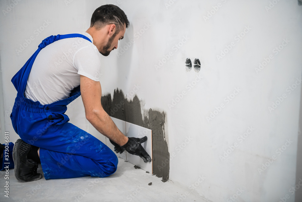 General laborerBuilder in overalls puts tiles on the bathroom wall General laborerBuilder in overalls puts tiles on the bathroom wall