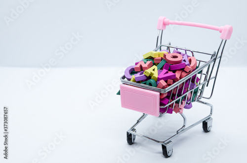 Multicolored wooden letters in a metal supermarket trolley on a white background. Concept: back to school, literacy, reading, language learning. Space for text
