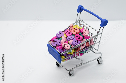 Multicolored wooden numbers in a metal supermarket trolley on a white background. Concept: back to school, math, arithmetic, learning to count. Space for text