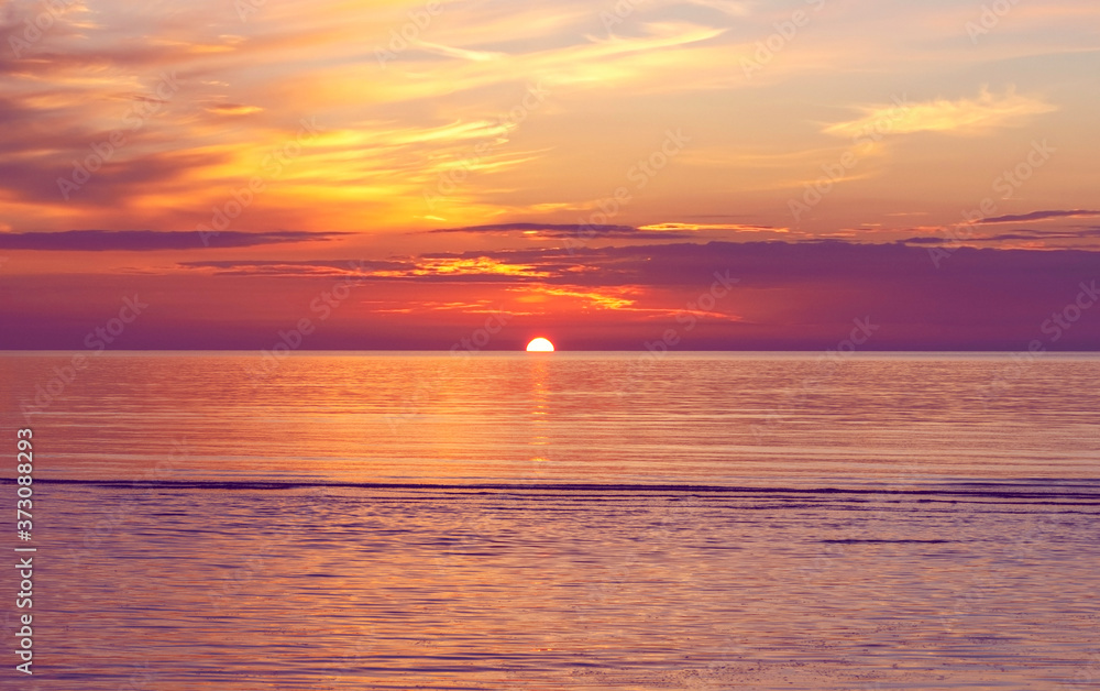 Summer colorful sunset with clouds at calm Baltic sea. Half of sun under horizon line.