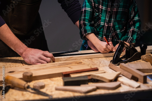 close-up of the work of a man and a boy at a carpenter's table, on the table are a plane, chisel, Board, workbench, ruler and other items.