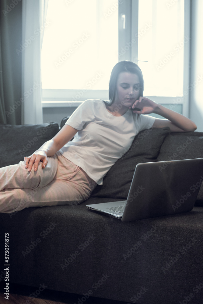 Young woman with modern laptop sitting on sofa at home Young woman with modern laptop sitting on sofa at home