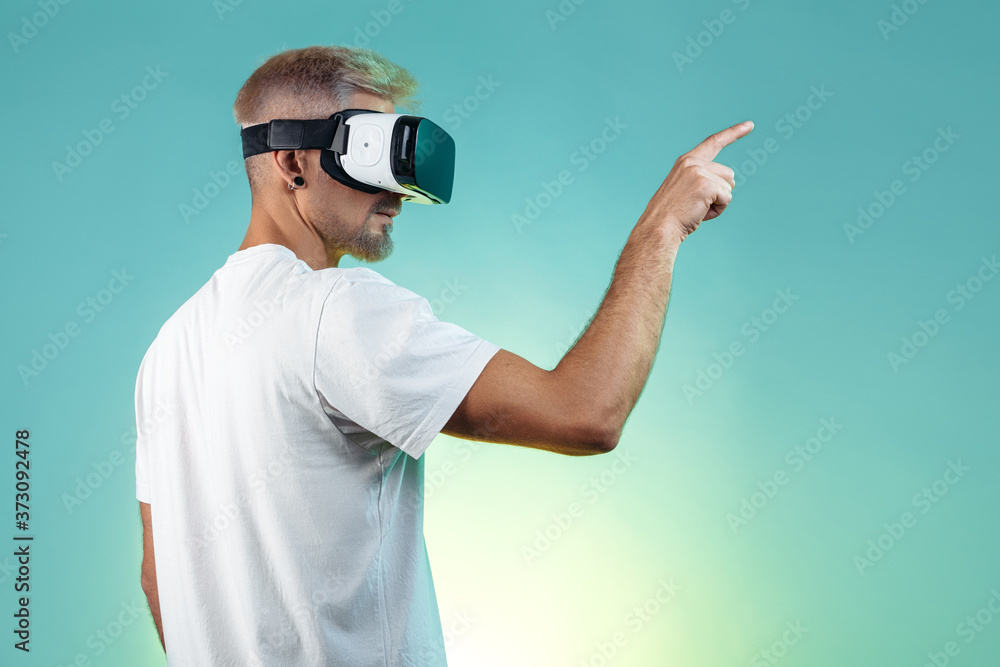 Handsome bearded hipster man wearing virtual reality goggles in studio in neon lights. Pointing finger. Handsome bearded hipster man wearing virtual reality goggles in studio in neon lights. Pointing finger.