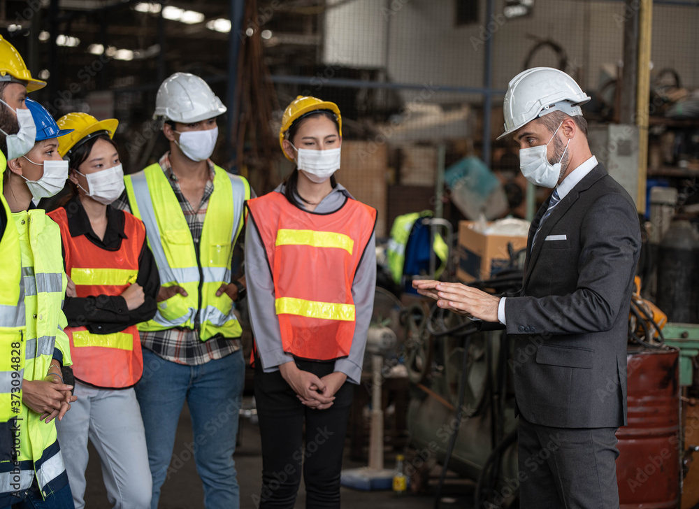 Group of factory workers consists of Manager, Engineers, Technicians with hardhat and vest jacket, discussing about industrial factory production management. They wear surgical Mask for covid 19 Group of factory workers consists of Manager, Engineers, Technicians with hardhat and vest jacket, discussing about industrial factory production management. They wear surgical Mask for covid 19