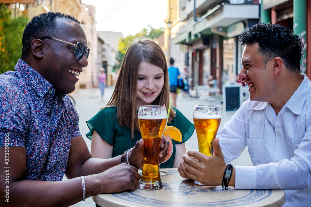 Multiracial group of friends drinking and toasting at street terrace of the cafe. Friendship concept with young multi ethnic people enjoying time together.