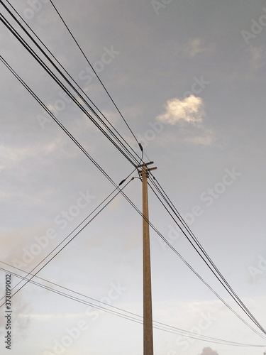 Wooden pole and electrical wiring under tropical gray sky. Chaos of telephone cables. Detail of Caribbean and tropical architecture and technology.