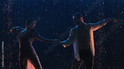Sensual passionate dance of a couple in love at night in the rain. Contact of wet hot bodies. Silhouettes of two lovers. A love story expressed in dance. Close up. Slow motion.