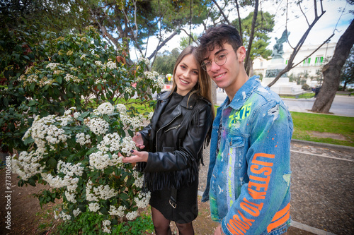 Outdoor, a young italian man and woman are couple in spring day in the park look over the hedge at the park flowers whit three and green whit flower photo