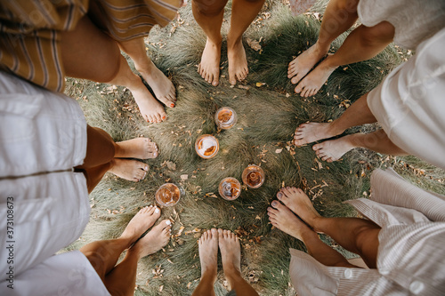 Female barefoot feet on dry grass standing in a circle with glasses of wine in the middle. photo