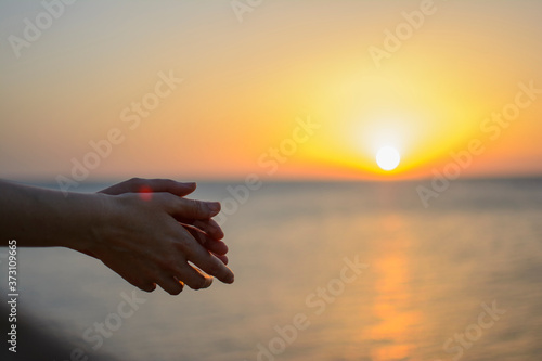 Crossed hands with the sea in the background in the sunset