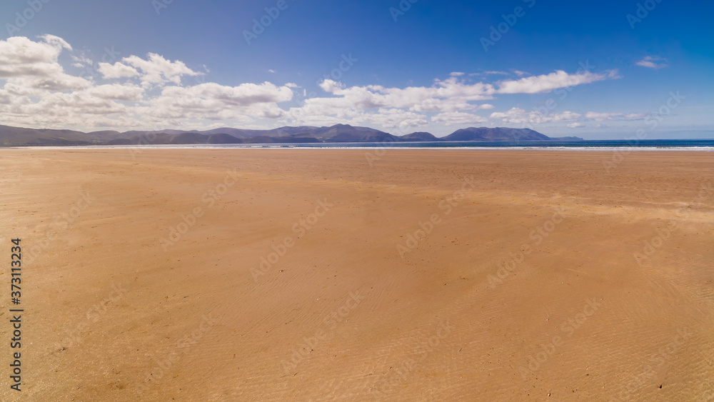Long, beautiful sandy Inch Beach with mountains in background. Summer day with blue sky on empty beach, relaxation. Dingle peninsula, Ireland