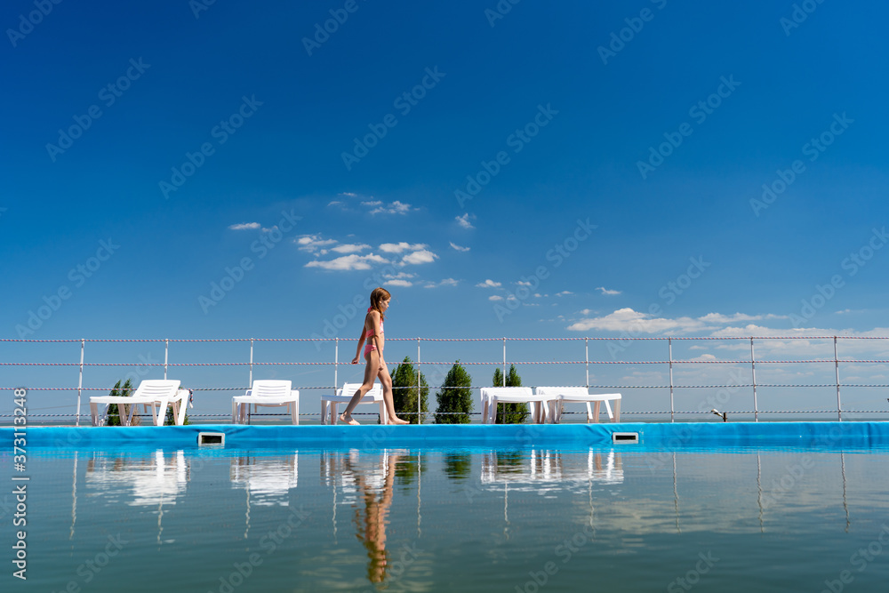 teenage girl in swimsuit goes along pool background sky