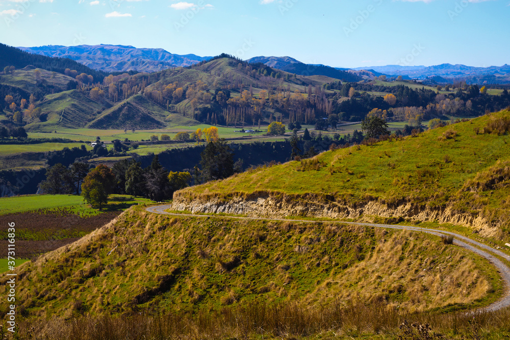 Road to Mountain and Landscape View. Blue Sky with Clouds, Hill, Yellow Trees, Green Grass and Village Background. Roadtrip to Highlands on Sunny Day in New Zealand. Rural Travel & Vacation Image.