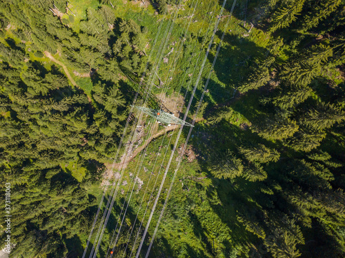 Aerial view of power line through alpine forest in Switzerland. Electric current distribution with power grid.