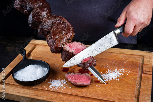 Traditional barbecue dry aged wagyu Brazilian picanha from the sirloin cap of rump beef sliced by a chef directly from the skewer as close-up on a wooden cutting board photo