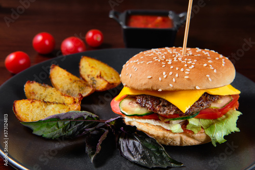 A classic burger with fresh herbs and a juicy cutlet. Close up view of fresh tasty beef burger and french fries with seasoning on rustic table.