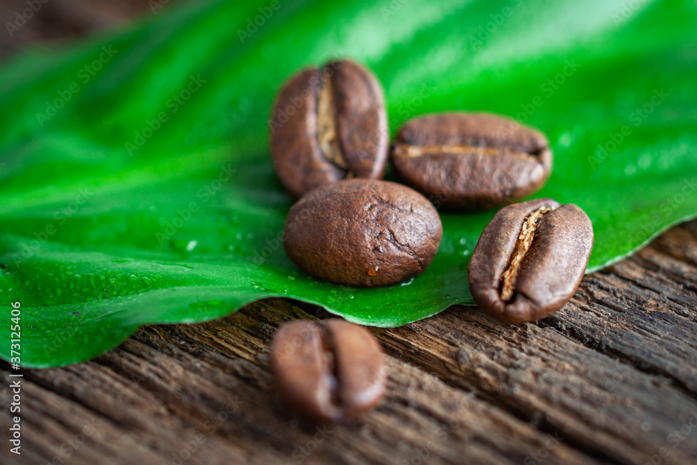 Fototapeta premium Coffee beans on a green leaf and wooden table