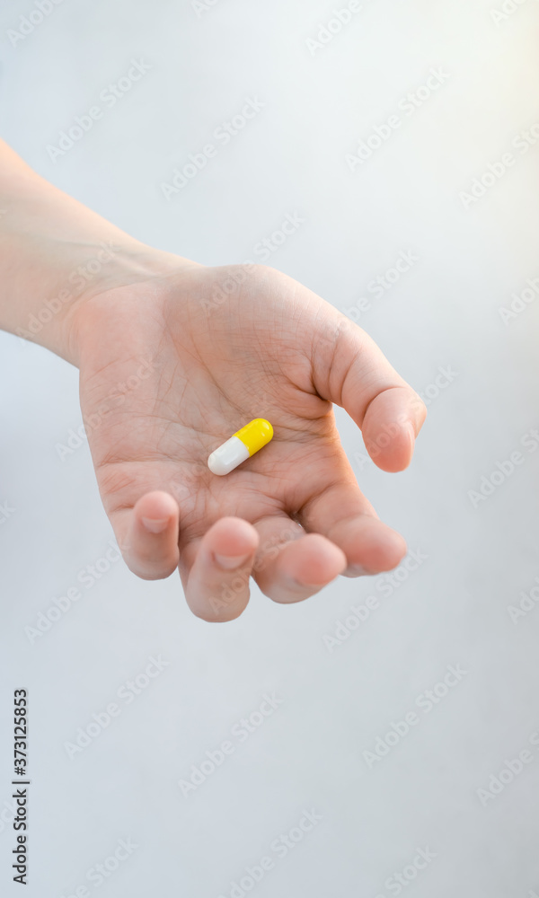 White-yellow pill in the form of a capsule lies in an outstretched female hand
