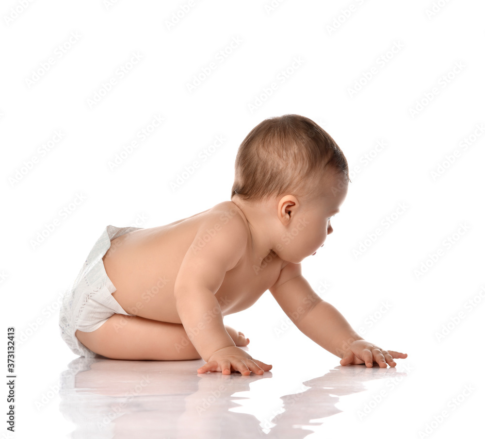 Infant baby toddler naked in diaper is sitting on floor side to us looking back touching catching something Infant baby toddler naked in diaper is sitting on floor side to us looking back touching catching something
