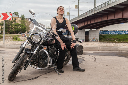 Long-haired guy on a black motorcycle under the bridge