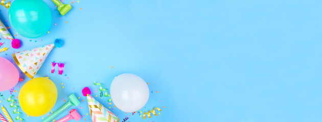 Birthday party banner with corner border on a blue background. Overhead view with confetti, balloons, party hats and streamers. Copy space.