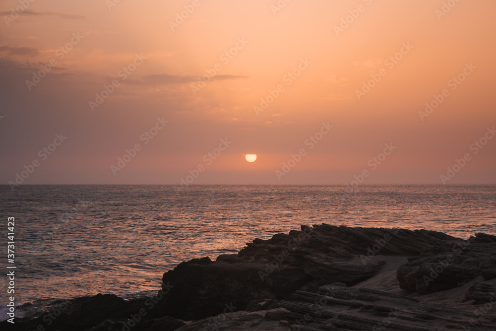 Beautiful sunset on the sea with the sun going down on the horizon and rocks in the foreground.