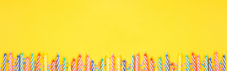 Birthday cake candles with candy sprinkles. Top down view banner with bottom border on a yellow background. Copy space.