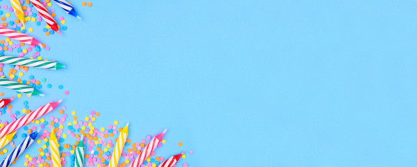 Birthday cake candles with candy sprinkles. Top view banner with corner border on a blue background. Copy space.
