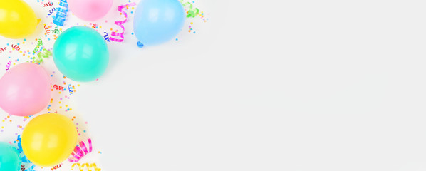 Birthday party theme banner with corner border on a white background. Overhead view with balloons, confetti and streamers. Copy space.