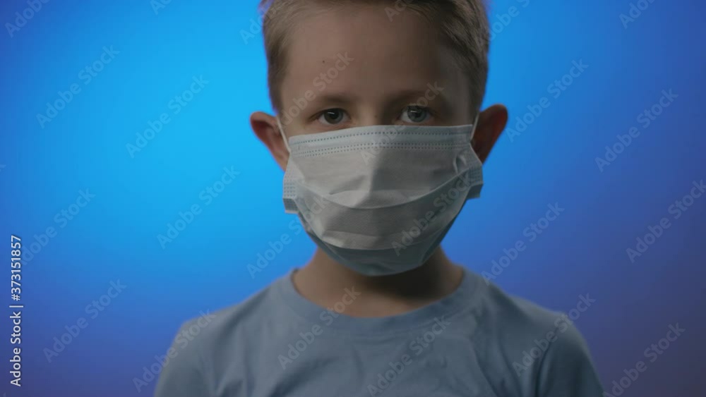A closeup portrait of a young man-child in a blue tee adjusting a virus mask in prevention of being infected by Covid19 A closeup portrait of a young man-child in a blue tee adjusting a virus mask in prevention of being infected by Covid19