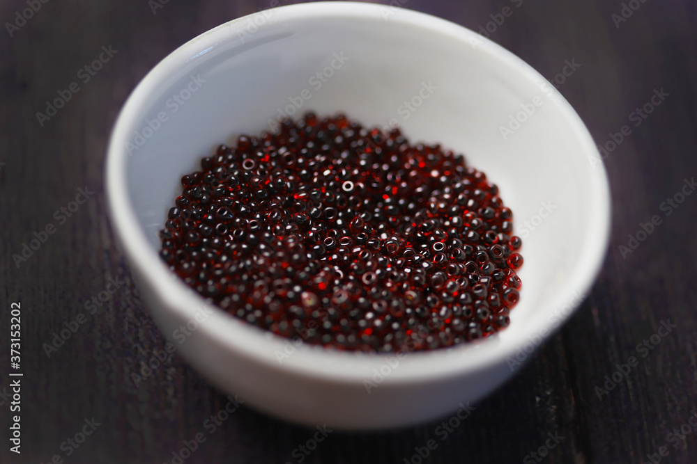 Dark red beads in a white cup on a black background Dark red beads in a white cup on a black background