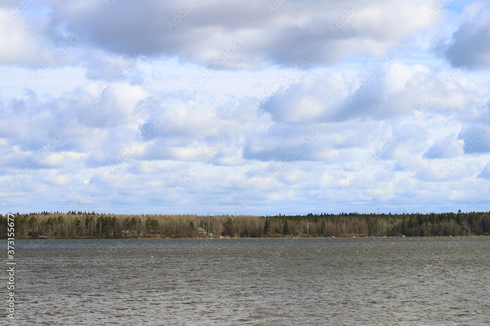 Landscape with a large lake and trees in the distance. The sky is in the clouds.