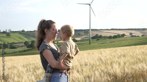 Mother holding her son as they smile and laugh together in a field. Wind turbine in the background showing hopeful future for the next generation