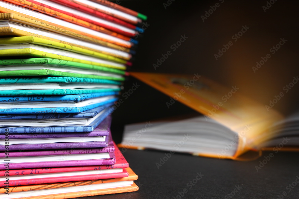 Domowa biblioteka - książki w kolorowych okładkach ułożone w kolumnie, otwarta książka w tle - obrazy, fototapety, plakaty 