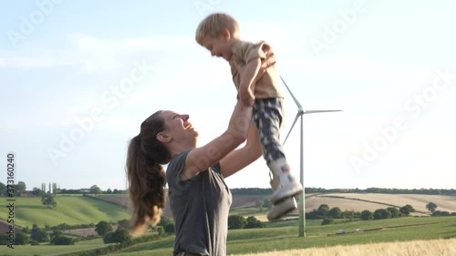Happy family concept, mother and son smiling and laughing as mother throws son in the air. Wind turbine in the background indicating a green energy future