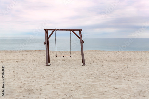 A large wooden swing on an empty beach against the background of the sea and sky © Ирина Трухина