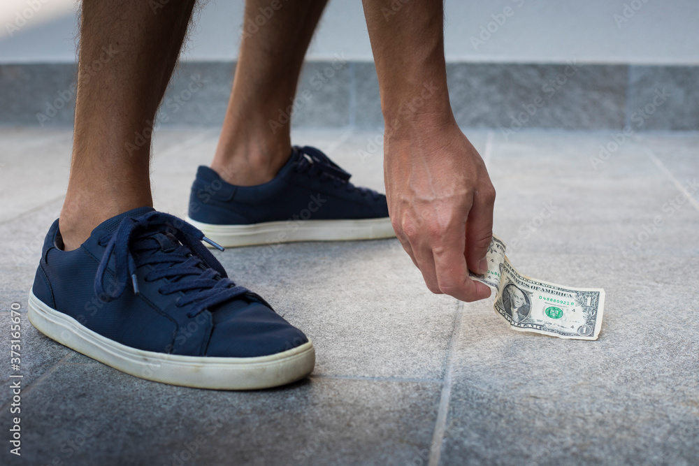 Anonymous man, casual dressed, with blue sneakers, picking up one dollar bill from the floor.