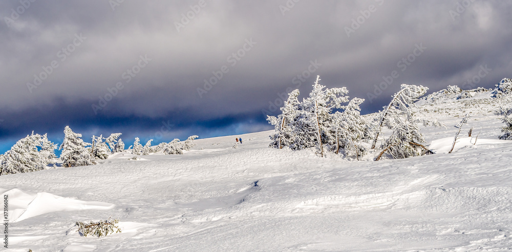 Two persons walking on the plato of the Ural mountains. It's sunny winter day but dark clouds are close to tourists