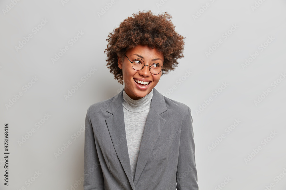 Cheerful prosperous businesswoman in elegant grey formal clothes, gazes happily aside, wears transparent glasses, feels successful to lead new project, accomplished business affairs, owns company - obrazy, fototapety, plakaty 