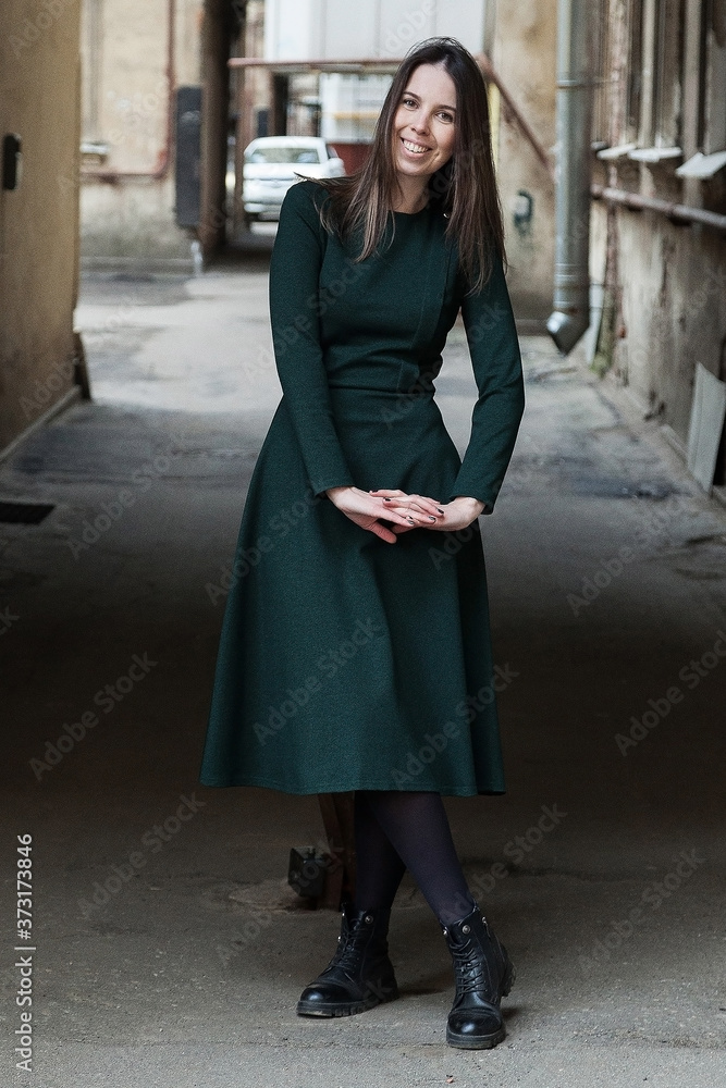 Fototapeta premium Stylish long-haired Girl in a long green dress is dancing in a shabby alleyway...Typical Petersburg courtyard