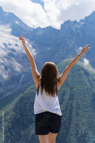 a girl stands in the mountains and raises her hands to the sky.
