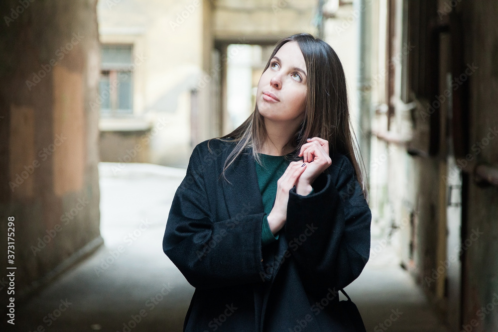 Fototapeta premium Long haired brown eyed girl in black coat portrait in a tyoicalsaint petersburg courtyard