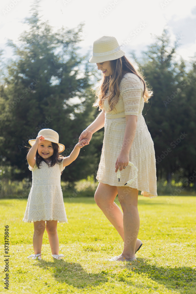 Hispanic girl holding her mother's hand in the park at sunset - Girl smiling watching the camera playing with her hat - Young Hispanic mother watching her adorable daughter with love