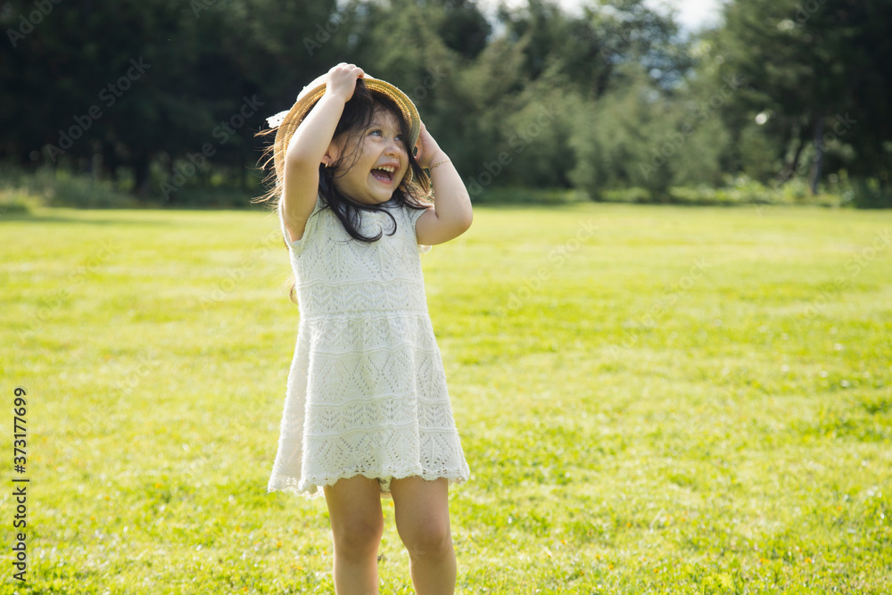 Obraz premium Little Hispanic girl smiling and playing in a natural park - little girl in a white dress and hat in the middle of a green field - cute little girl playing with her hat.