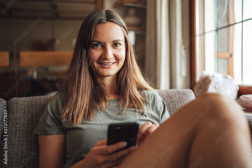 Portrait of beautiful young woman holding mobile phone while sitting on sofa in living room Portrait of beautiful young woman holding mobile phone while sitting on sofa in living room